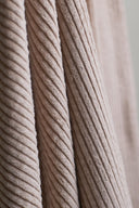 Gros plan sur les larges côtes du velours côtelé beige rosé, drapé en plis verticaux.