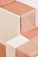 Tissu velours côtelé rose saumon plié, avec des boutons assortis dans une coupelle en céramique.