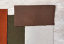 Coupons de tissus rouille, vert olive, marron et écru superposés sur une pierre claire – Nouvelle collection Atelier Brunette
