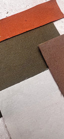 Coupons de tissus rouille, vert olive, marron et écru superposés sur une pierre claire, cadrage vertical – Nouvelle collection Atelier Brunette