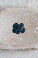 Boutons ronds classiques à deux trous, finition mate bleu-vert forêt très foncé, présentés en tas sur une pierre beige marbrée.
