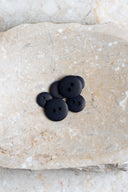Boutons ronds classiques à deux trous, finition mate bleu marine très sombre (night), présentés en tas sur une pierre beige marbrée.