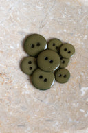 Boutons ronds classiques à deux trous, finition brillante vert olive kaki, présentés en tas sur une pierre beige marbrée.