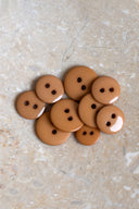 Boutons ronds classiques à deux trous, finition brillante ocre caramel, présentés en tas sur une pierre beige marbrée.