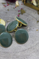 Same faceted cedar green Gem buttons, close-up from a different angle showing the gold sewing shank ring on the back of one button.