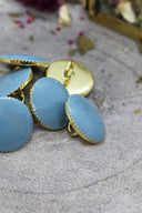 Extreme close-up of the same faceted Gem buttons in blue-grey with a gold trim, from a different angle.