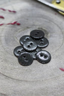 Fully glittered two-hole round buttons in black, piled on grey stone, with a strand of burgundy raffia in the background.