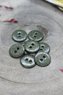 Fully glittered two-hole round buttons in khaki green, piled on grey stone, with a strand of burgundy raffia in the background.