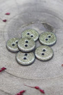 Gros plan sur les boutons entièrement pailletés, vue rapprochée mettant en valeur le grain scintillant de la finition.