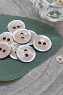 Gros plan sur les mêmes boutons émaillés cerclés de nacre, vue rapprochée révélant la texture brillante et le liseré blanc.