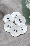 Gros plan sur les mêmes boutons émaillés cerclés de nacre, vue rapprochée révélant la texture brillante et le liseré blanc.
