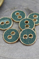 Sept petits boutons ronds à deux trous, finition pailletée dorée sur fond vert cactus, cerclés d'un liseré métallique doré, photographiés en gros plan sur une pierre grise.