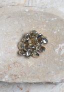 Domed, pebble-shaped round buttons with a shiny, reflective gold metallic finish, piled on marbled beige stone.