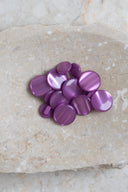 Boutons ronds bombés à queue, sans trous apparents, finition nacrée rose fuchsia vif bubble-gum, présentés en tas de tailles variées sur une dalle de pierre beige marbrée.