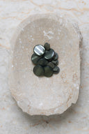 Domed round shank buttons with no visible holes, pearly greyish cedar green finish, piled in various sizes in an oval marbled beige stone dish.