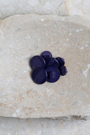 Domed round shank buttons with no visible holes, pearly cobalt navy blue finish, piled in various sizes on a slab of marbled beige stone.