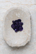 Domed round shank buttons with no visible holes, deep pearly violet finish, piled in various sizes in an oval marbled beige stone dish.