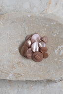 Boutons ronds bombés à queue, sans trous apparents, finition nacrée beige rosé sable, présentés en tas de tailles variées sur une dalle de pierre beige marbrée.