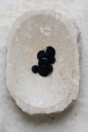 Domed round shank buttons with no visible holes, deep pearly black (night) finish, piled in various sizes in an oval marbled beige stone dish.