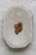 Boutons ronds bombés à queue, sans trous apparents, finition nacrée brun caramel pecan pie, présentés en tas de tailles variées dans une coupelle en pierre ovale beige marbrée.