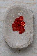 Boutons ronds bombés à queue, sans trous apparents, finition nacrée rouge orangé translucide, présentés en tas de tailles variées dans une coupelle en pierre ovale beige marbrée.