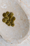 A dozen small glossy two-hole round buttons in dreamy twilight khaki olive green, piled in a marbled beige stone dish.