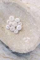 A dozen small glossy two-hole round buttons in pearly off-white, piled in a marbled beige stone dish.
