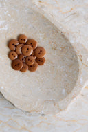 A dozen small glossy two-hole round buttons in pecan pie caramel brown, piled in a marbled beige stone dish.