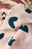 Tissu Oasis rose poudré à motif de formes organiques abstraites marine et écru, plié sur un support en bois devant un fond terracotta.