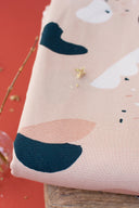 Tissu Oasis rose poudré drapé en plis souples, motif de formes organiques marine et écru, avec des brindilles séchées dorées à proximité.