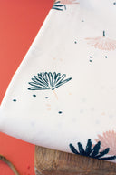 Tissu Palmetto ivoire plié en plusieurs épaisseurs, laissant apparaître le motif de feuilles de palmier marine et rose poudré près de brindilles séchées.