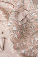Petal fabric in off-white with a graphic leaf pattern in terracotta and sage, folded with a dried ginkgo leaf placed on top.