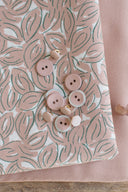 Petal fabric in off-white, folded, with powder pink and pearly buttons scattered over the leaf pattern.