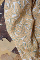Petal fabric in mustard, folded and placed on a wooden tray with dried autumn leaves nearby.