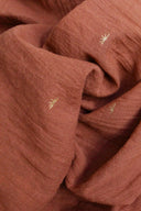 Gros plan sur la gaze de coton Sunset terracotta, détaillant la broderie dorée en forme de soleil.
