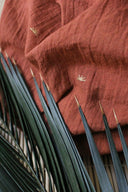 Tissu Sunset terracotta drapé avec des épis de blé séchés posés dessus, mettant en valeur la légèreté de la gaze.