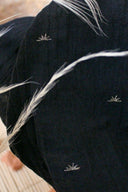 Tissu Sunset marine en gaze de coton semi-transparente à motifs soleil brodés blanc argenté, avec une plume claire posée dessus.
