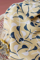 Windy fabric in mustard draped in soft folds, revealing the full curved-leaf pattern in navy, with a terracotta background.