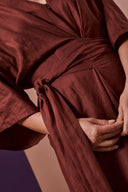 Combi Addie pattern – detail of the tied belt, burgundy jumpsuit, hands holding the ties – Atelier Brunette