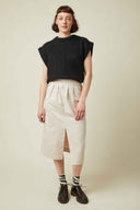 Défendue Skirt pattern – front view, midi skirt off-white, front slit, black top, beige background – Atelier Brunette