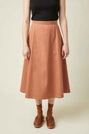 Patron La Jupe – Plan corps, jupe midi ample terracotta taille haute évasée, sabots cognac, fond beige – Atelier Brunette