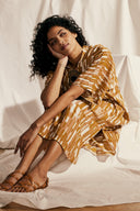 Tunic Dress pattern – Woman seated, tunic dress terracotta/gold geometric print, cream fabric background – Atelier Brunette