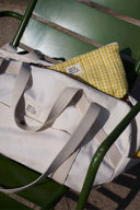 Escapade Pack pattern – travel bag and bum bag yellow gingham, placed on a green chair – Atelier Brunette