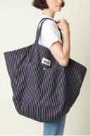 Patron Sac de plage – Femme de profil portant sac oversize rayé marine/blanc, anse épaule, fond beige – Atelier Brunette