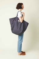 Patron Sac de plage – Femme de profil, sac rayé marine/blanc porté deux épaules, sabots bois, fond beige – Atelier Brunette