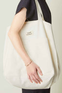 Patron Sac de plage – Femme tenant sac de plage oversize blanc crème de côté, fond beige – Atelier Brunette