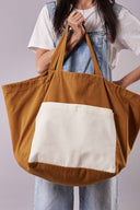 Patron Sac de plage – Femme portant sac oversize bicolore caramel/crème devant elle, fond lilas/mauve – Atelier Brunette