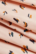 Autre vue du tissu plié en plis serrés, montrant l'imprimé confettis sur fond rose poudré.