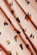 Gros plan sur un tissu viscose rose poudré à imprimé confettis graphiques (formes géométriques marine, terracotta et blanc cassé), plié en plis souples.