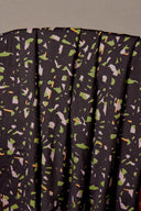 Tissu viscose Candy Rock noir à imprimé confettis graphiques vert et lilas, drapé sur l'accoudoir en bois d'une chaise vintage.